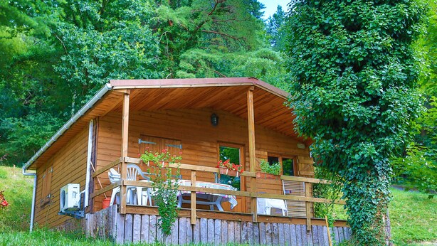 Una cabaña de madera con porche, rodeada de abundante vegetación.