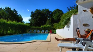 Una piscina con borde de baldosas, rodeada de vegetación y un muro blanco.
