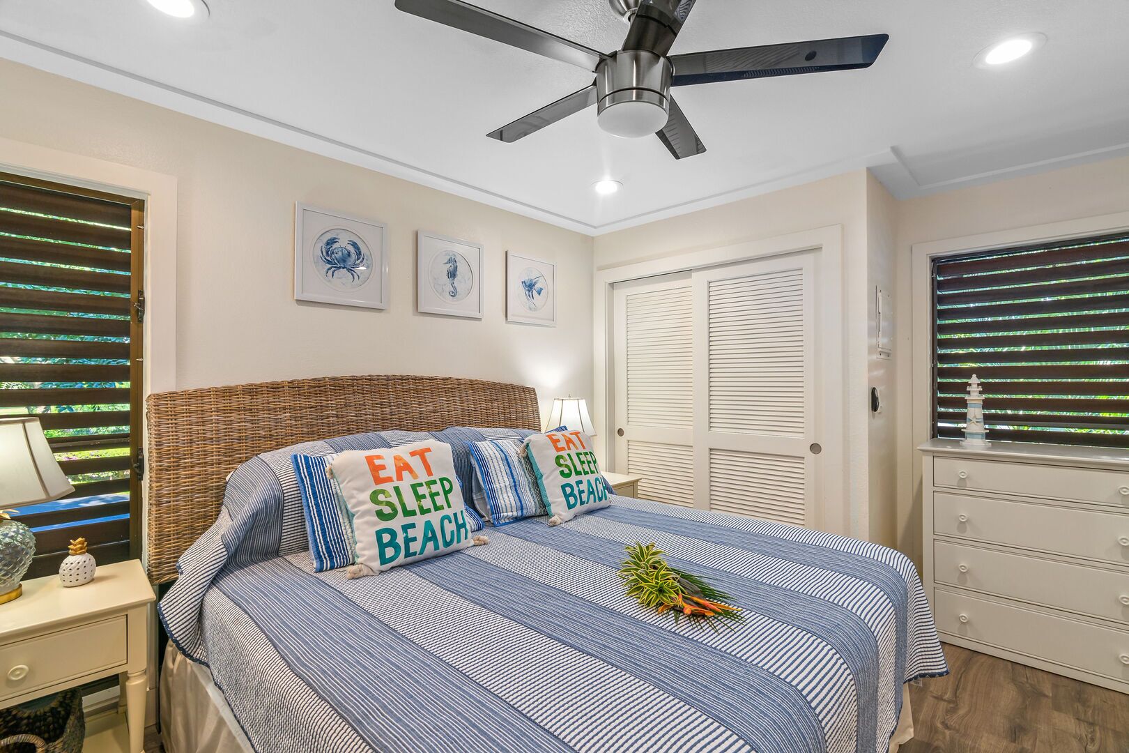 A bedroom with a bed, a nightstand, a lamp, a ceiling fan, and a dresser.