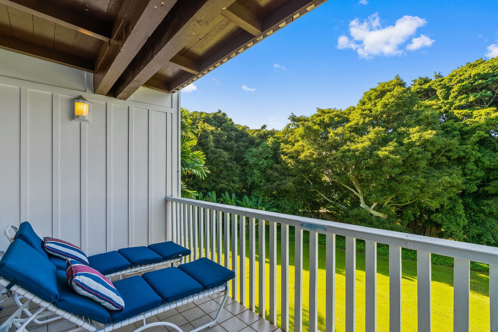 Un balcon avec des balustrades blanches et des chaises bleues dotées de coussins.
