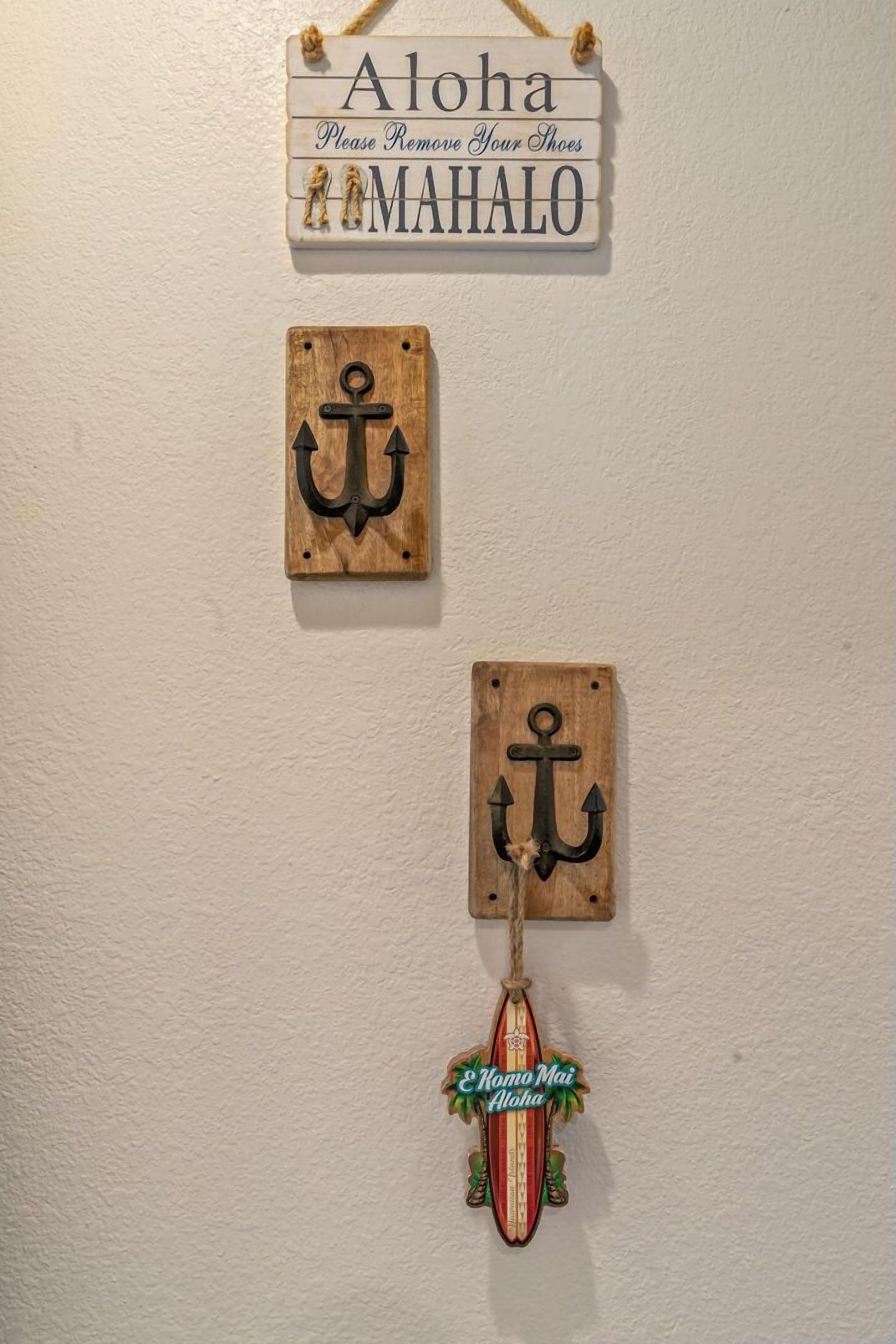 A wall with three wooden signs: one with 'Aloha Please Remove Your Shoes MAHALO' and two with anchor symbols.