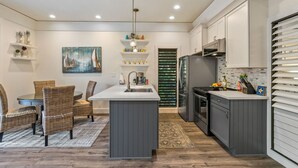 A modern kitchen with grey cabinets, a central island, and a dining area with wicker chairs.