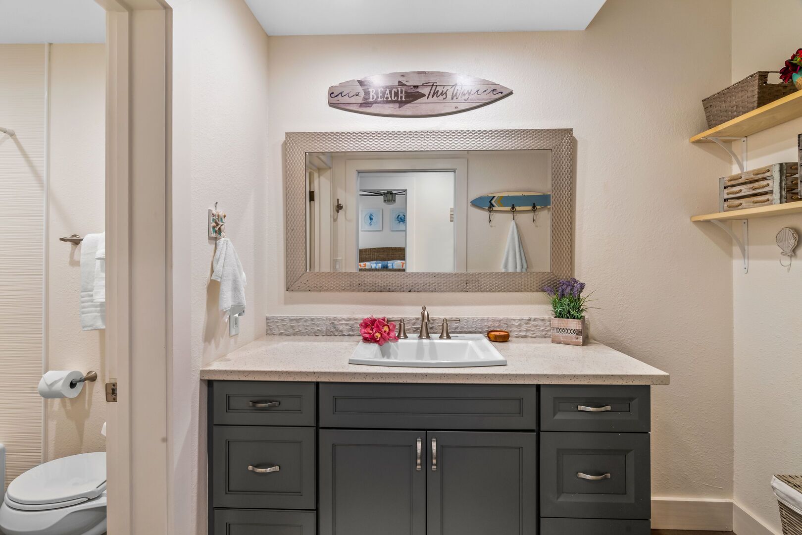 A bathroom with a vanity, mirror, and a shelf with decorative items.