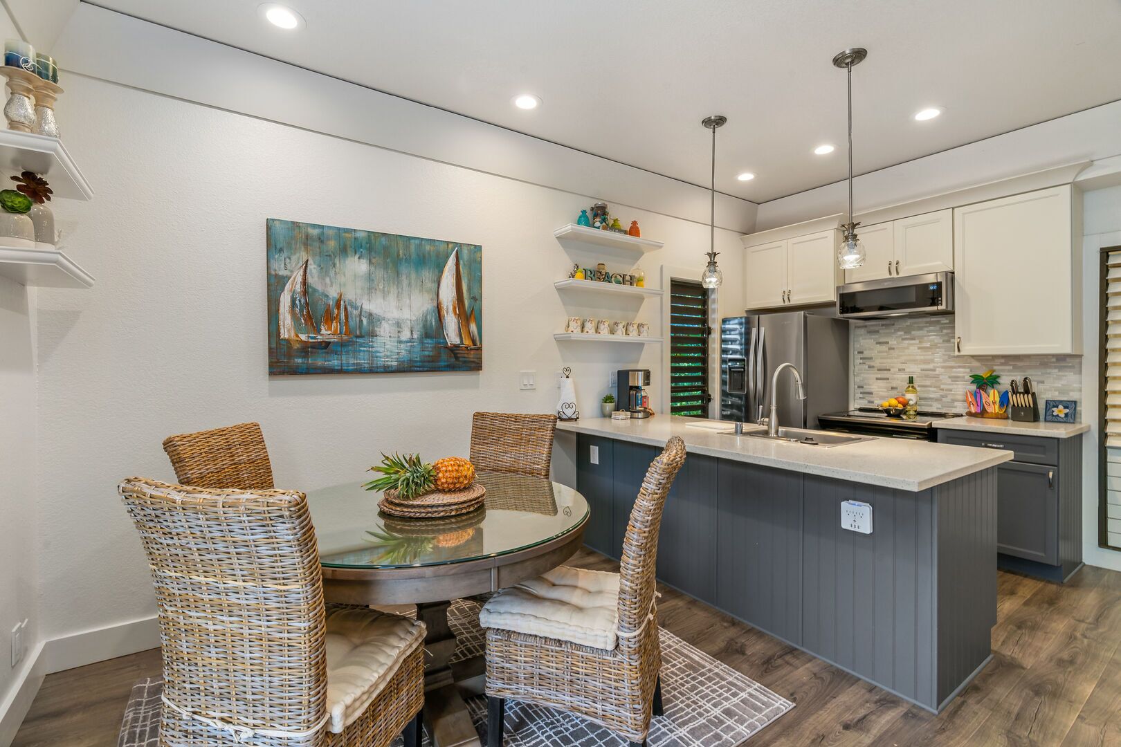 Una cocina moderna con una isla central, comedor con sillas de mimbre y un cuadro en la pared.