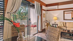 A room with a glass door leading to a balcony, a sofa, a table with a vase, and a lamp.