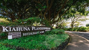 A sign for Kiahuna Plantation Resort with a restaurant and bar, surrounded by lush greenery and trees.