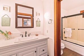 Une salle de bain avec un meuble-lavabo blanc, un grand miroir, une douche avec une porte en verre et des toilettes.
