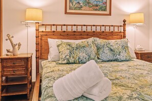 Un lit bien fait, avec une literie à motifs floraux, deux lampes de chevet, une tête de lit en bois et un petit objet décoratif posé sur la table de chevet.