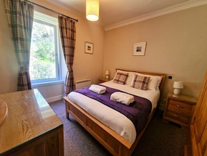 Une chambre à coucher avec un lit en bois, deux tables de chevet, une fenêtre avec des rideaux et un bureau.