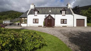 A white stone house with a dark roof, a central entrance, and a gravel driveway. - Rowan Cottage - Retreat Group (Aviemore)