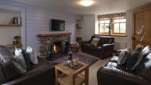 A cozy living room with a stone fireplace, leather sofas, a flat-screen TV, and a window with a view. - Rowan Cottage - Retreat Group (Aviemore)