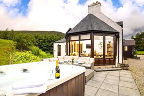 A cozy outdoor seating area with a hot tub, a bottle of champagne, and a table set for two. - Rowan Cottage - Retreat Group (Aviemore)