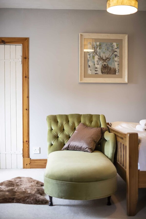 A green upholstered armchair with a brown pillow, a framed painting of a deer, and a wooden door. - Rowan Cottage - Retreat Group (Aviemore)