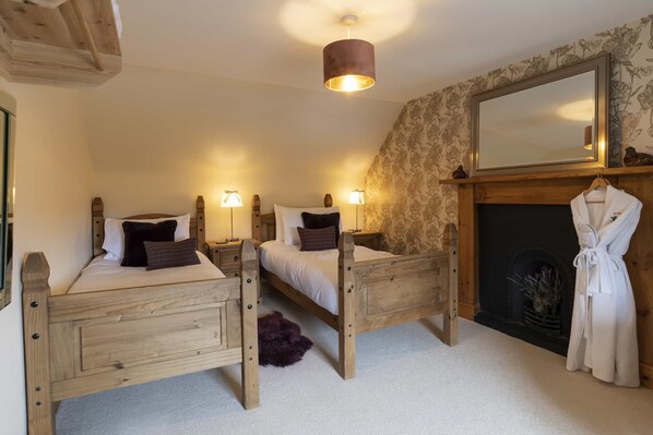 A bedroom with two wooden beds, a fireplace, a mirror, and a robe hanging on the wall.