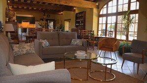 A spacious living area with a sofa, armchairs, a glass coffee table, and a kitchen in the background. - Les Granges du Château : Charming gîte with swimming pool in Burgundy (Chevannes)