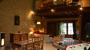 A rustic interior with a dining area, sofas, a foosball table, and a staircase leading to an upper level. - Les Granges du Château : Charming gîte with swimming pool in Burgundy (Chevannes)