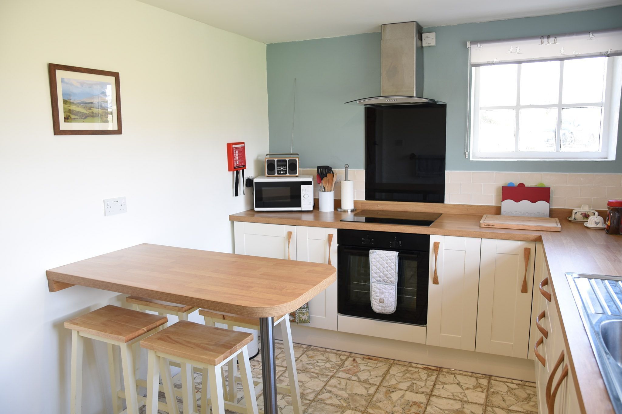 A kitchen with a wooden table and stools, a microwave, oven, and a window with curtains.