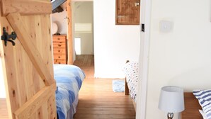 Una camera da letto con una porta in legno, un comodino con una lampada, un letto con copripiumino a righe e un pavimento di legno.