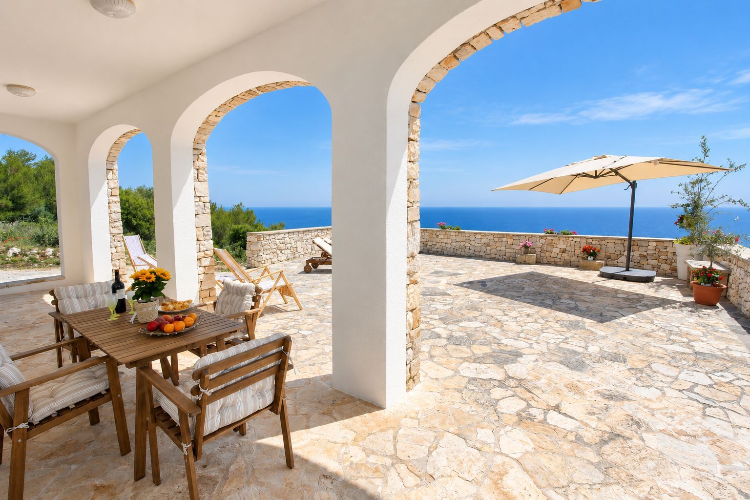 A stone patio with a table and chairs, a sun umbrella, and a view of the sea.