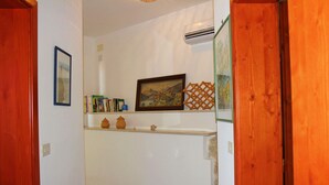 Un corridoio con una parete bianca, un quadro incorniciato e uno scaffale con libri e oggetti decorativi.