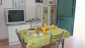 Zona pranzo con tavolo apparecchiato per quattro, televisione, forno a microonde e mobiletto con ripiani.