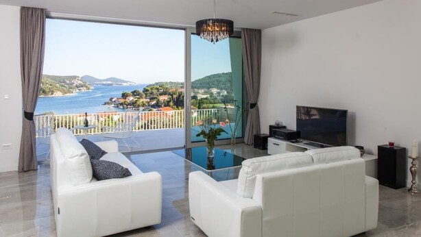 Ein modernes Wohnzimmer mit einem großen Glasfenster, das auf einen Balkon mit Meerblick führt.