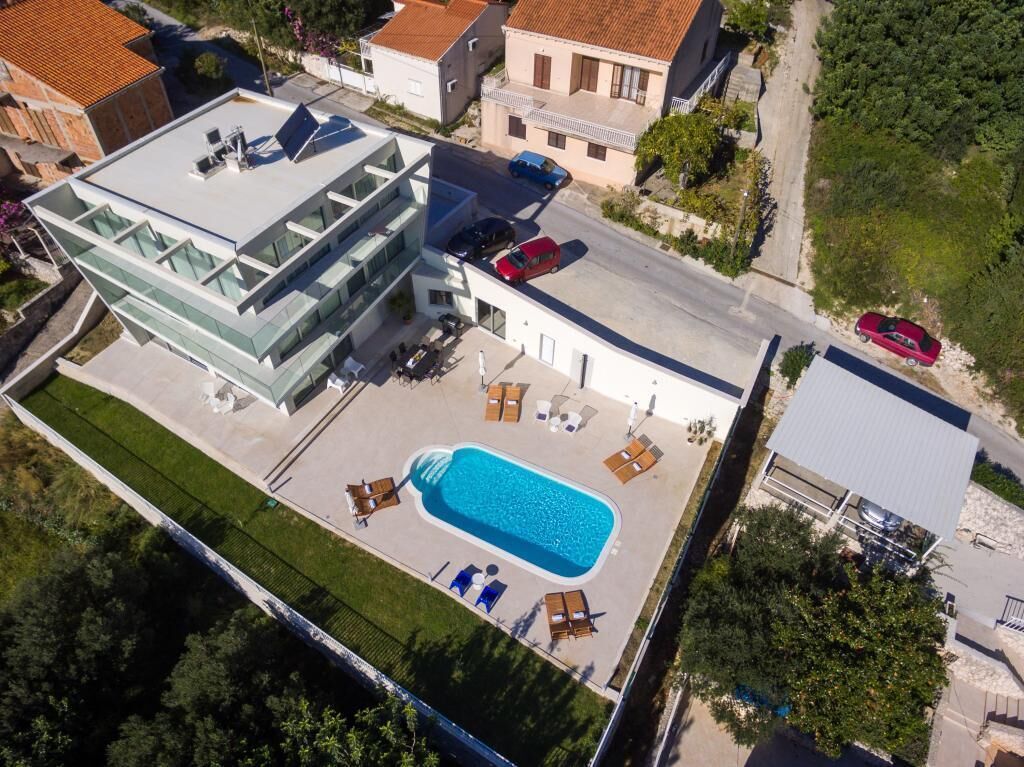 Vue aérienne d’une maison moderne dotée d’une piscine, d’un patio couvert et d’un garage.