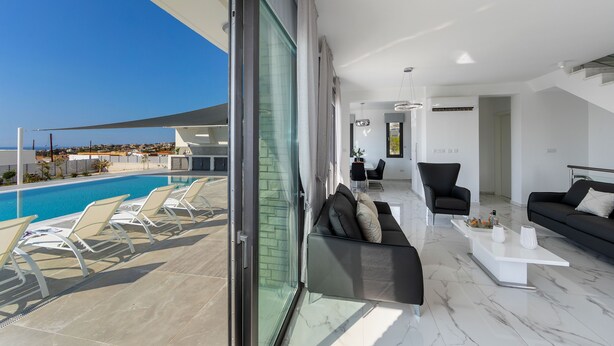 A modern living room with a pool view, a sofa set, and a coffee table. - Villa Andromeda Sea Caves (Paphos)
