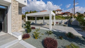 A modern outdoor patio area with a white pergola, stone wall, and landscaped garden with various plants. - Villa Andromeda Sea Caves (Paphos)