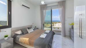 A modern bedroom with a large bed, a view of the sea, and a balcony. - Villa Andromeda Sea Caves (Paphos)