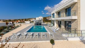 A modern pool area with lounge chairs and a clear view of the surrounding landscape. - Villa Andromeda Sea Caves (Paphos)