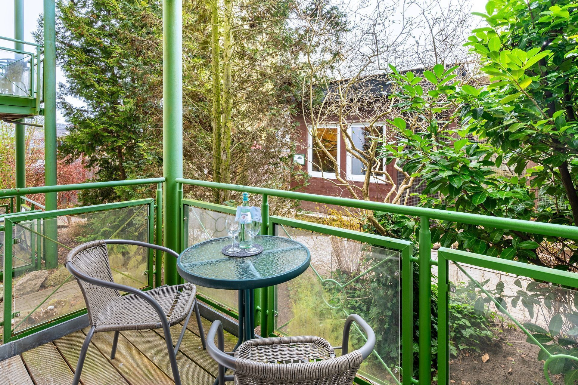 A balcony with a table and chairs, overlooking a garden and a building.