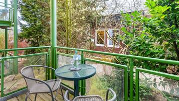 A balcony with a table and chairs, overlooking a garden and a building.