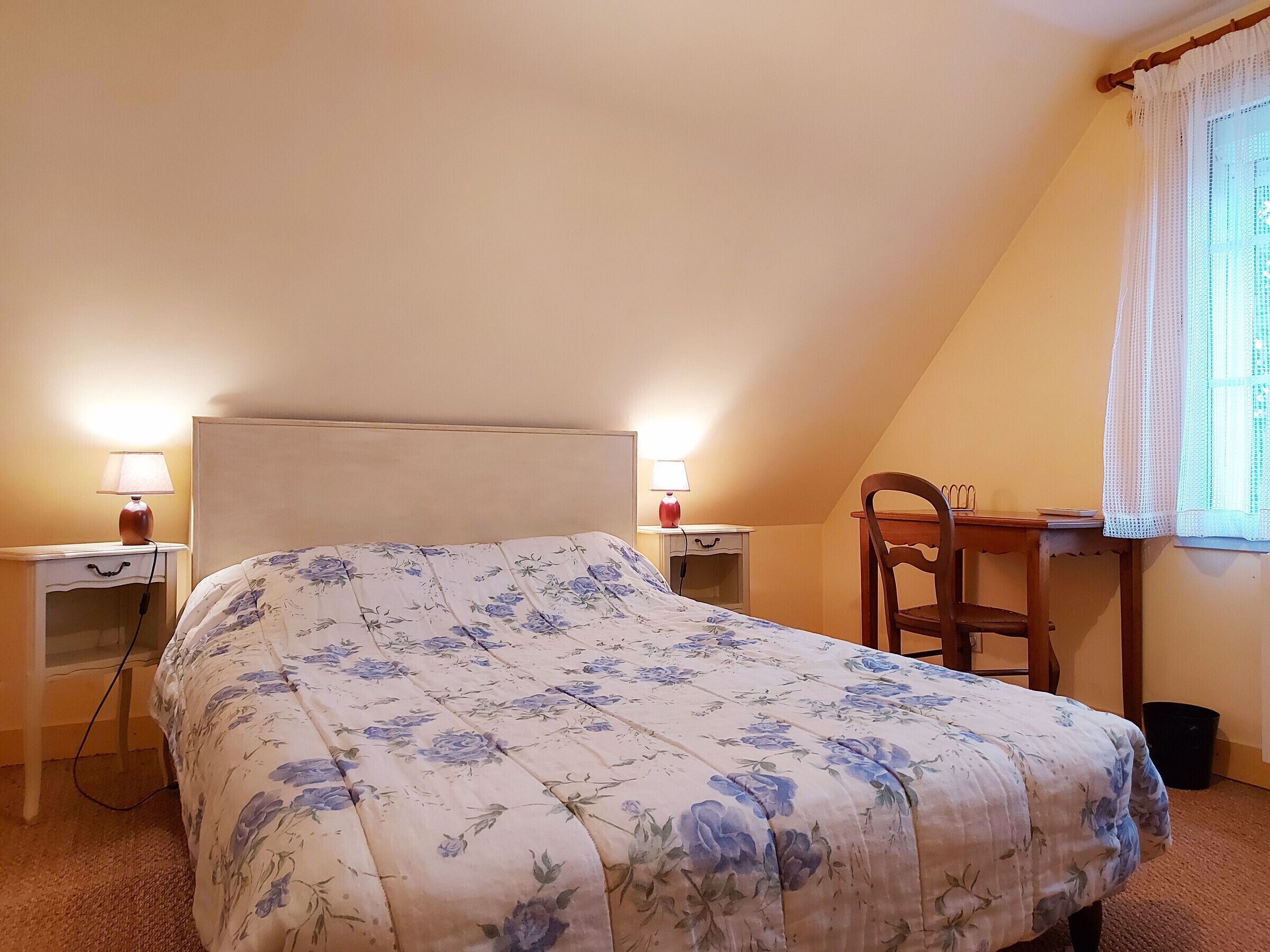 Een slaapkamer met een bed, twee nachtkastjes, een stoel, een bureau en een raam met gordijnen.