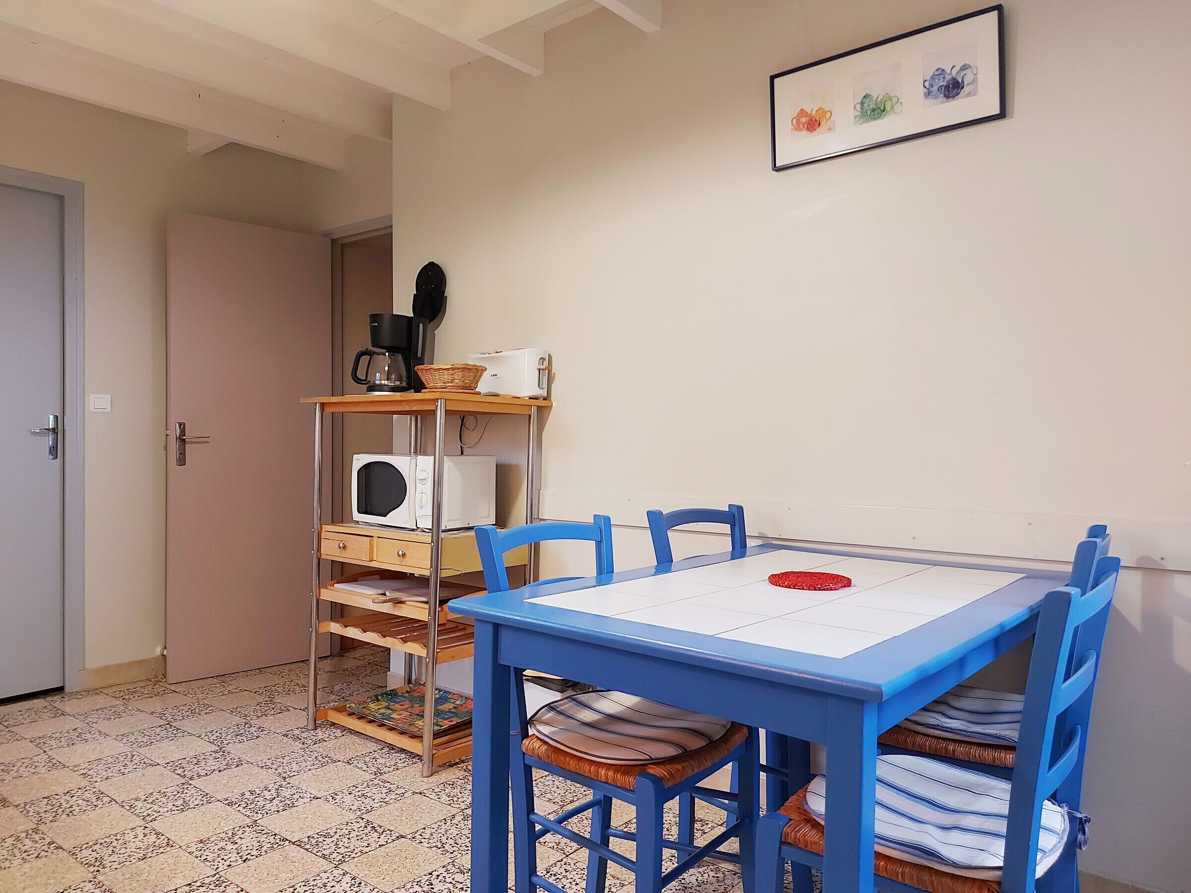 A room with a blue table and chairs, a white microwave, a toaster, and a basket on a shelf.