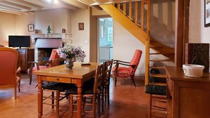 Un área de comedor con una mesa y sillas de madera, un florero con flores y una escalera que sube a otro nivel.