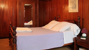 Een slaapkamer met houten lambrisering, een bed, nachtkastje, lamp en een ingelijst beeld aan de muur.