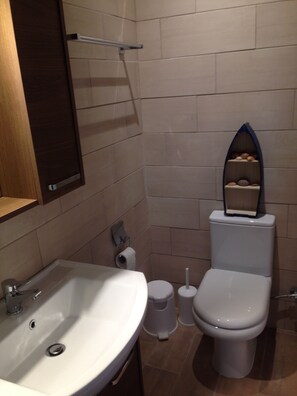 A bathroom with a white sink, toilet, and a shelf with toiletries. - The Fisherman's Cottage (Corfu)