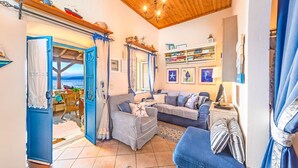 A cozy living room with a view of the sea, a blue door, and a bookshelf. - The Fisherman's Cottage (Corfu)