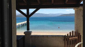 A wooden pier extending into a clear blue sea with mountains in the background. - The Fisherman's Cottage (Corfu)
