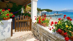 A coastal property with a wooden gate labeled "AGNI COTTAGE," outdoor seating, and a view of the sea and boats. - The Fisherman's Cottage (Corfu)