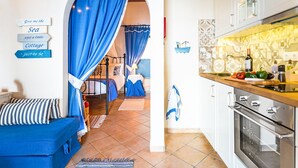 A cozy room with a bed, a blue sofa, and a kitchen area with a stove and counter. - The Fisherman's Cottage (Corfu)