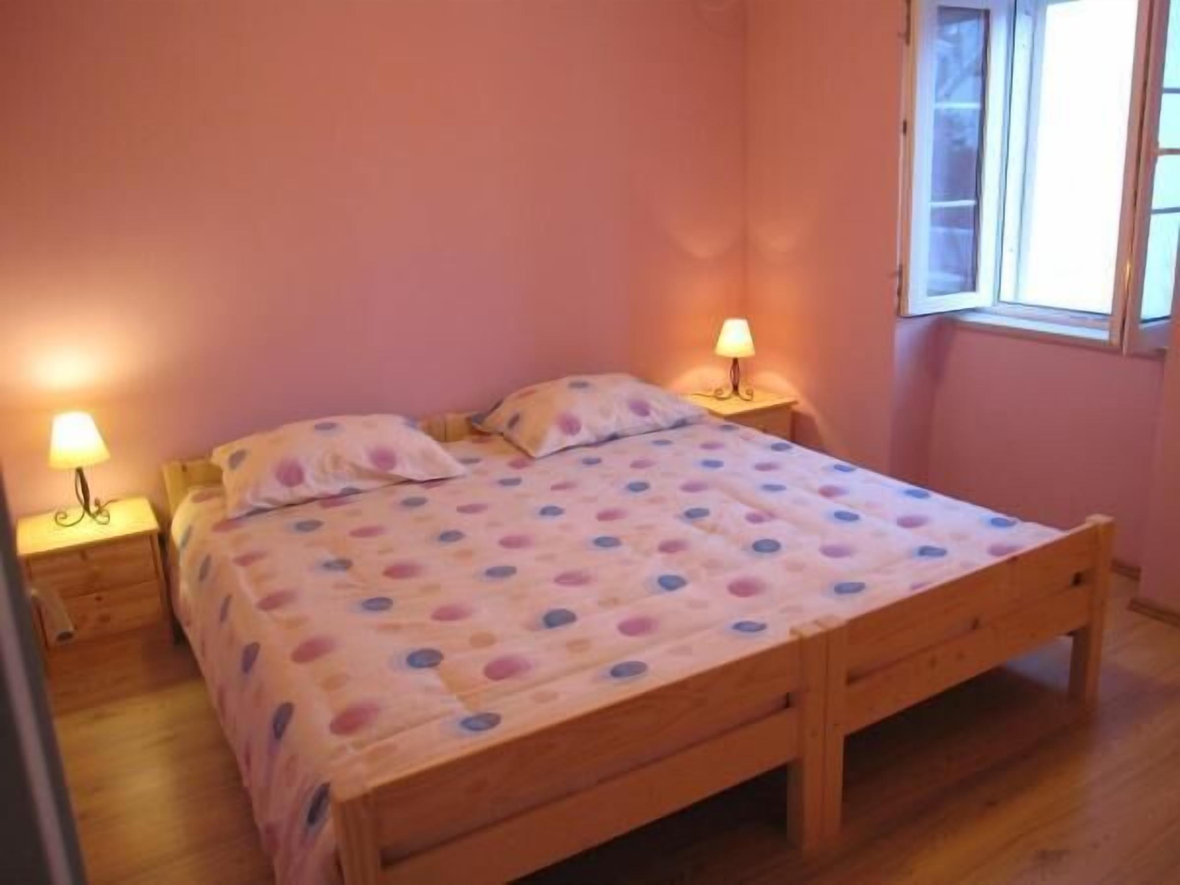 Quarto com cama de madeira, duas mesas de cabeceira com luminárias e uma janela com vista.