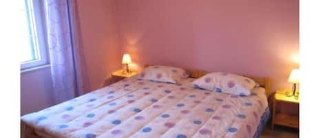 A single bed with a polka dot bedspread, two bedside lamps, and a window with curtains.