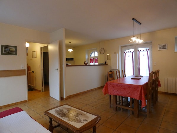 Un'area pranzo con tovaglia rossa, sedie di legno, pavimento piastrellato e una cucina sullo sfondo.