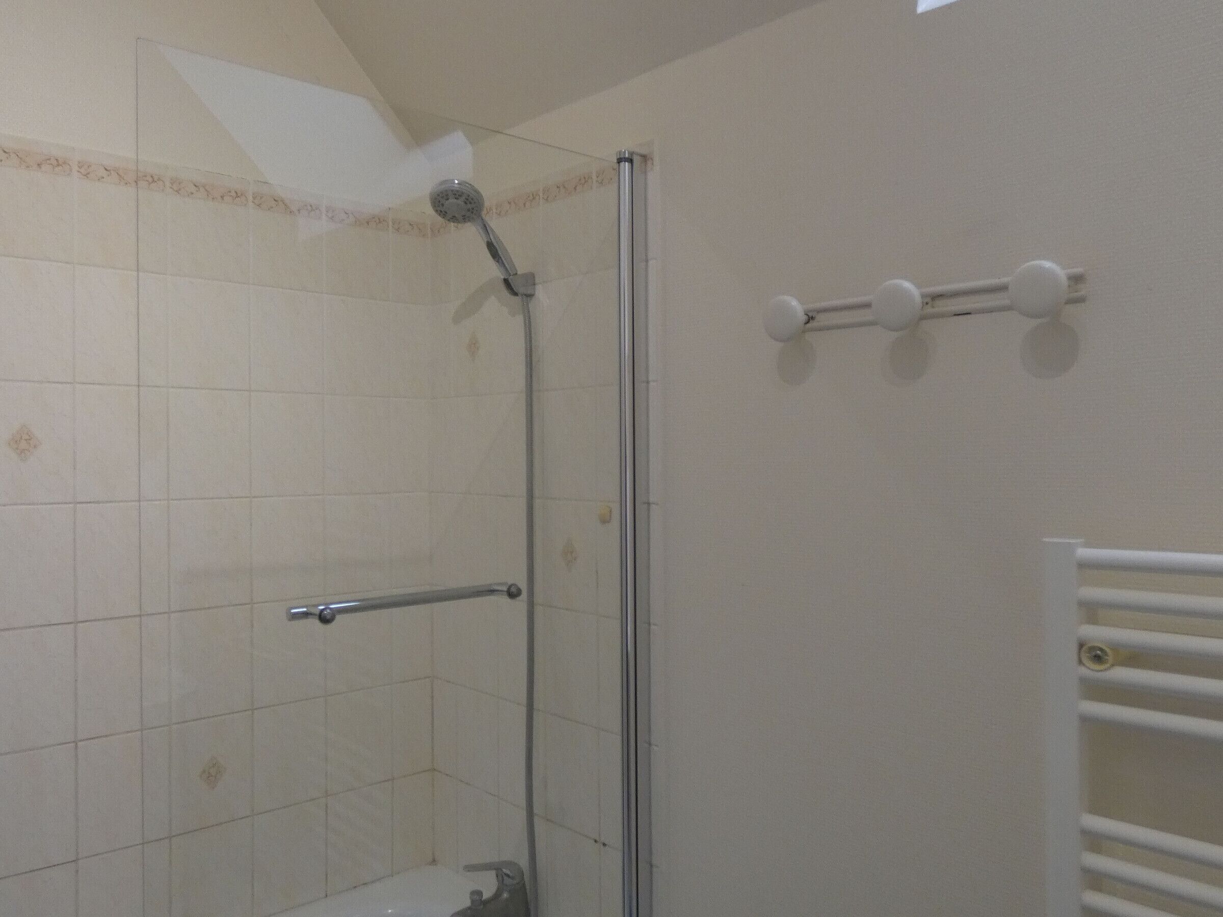 A shower with a glass door, a towel rack, and a white towel rack on the wall.