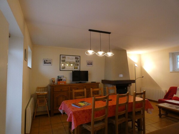 A dining area with a table set for four, a television on a stand, and a fireplace. - Charming 3-Bedroom Cottage in Trizay-Coutretot-Saint-Serge, Pet-Friendly, Near Outdoor Activities (Trizay-Coutretot-Saint-Serge)