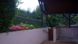 Un patio cubierto con una mesa y sillas, rodeado por un muro bajo y diversas plantas en flor.