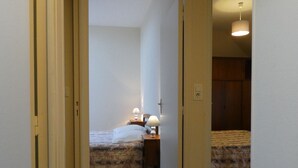 Un pasillo estrecho que conduce a un dormitorio con cama, mesita de noche y lámpara.