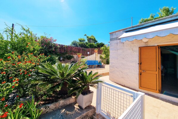A residential property with a gated entrance, a small patio area, and a view of a blue bench and trees in the background.